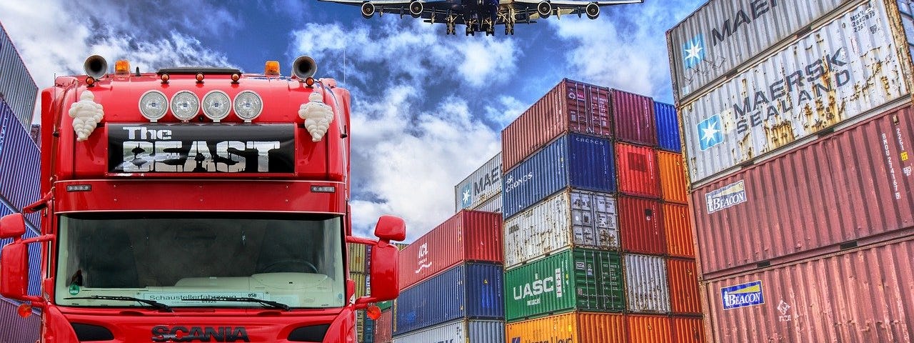 IMAGE: A big truck, a pile of containers and a plane passing by