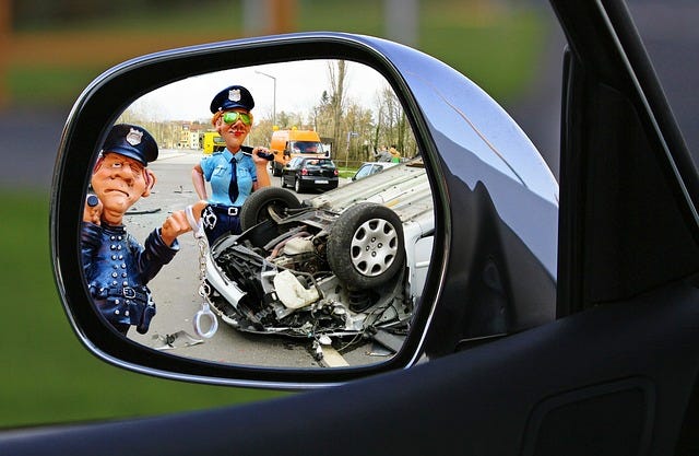 Photo of a car crash scene with police on site. Seen through the reflection of a car’s side mirror.